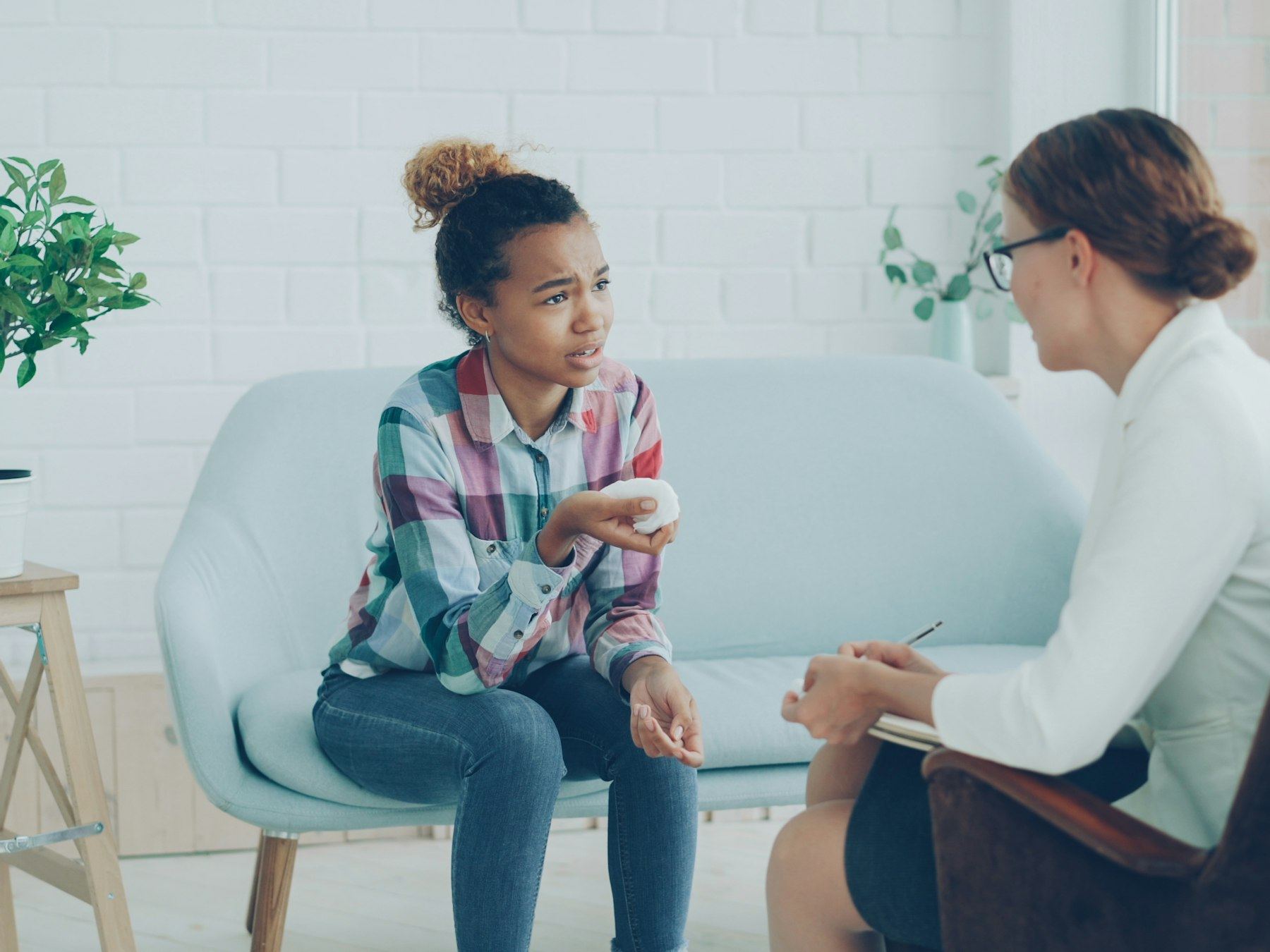 A woman talks with a young girl seated on a couch in a bright room.